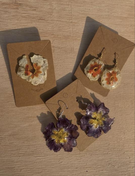 Orecchini con fiori pressati arancio e viola su un tavolo di legno