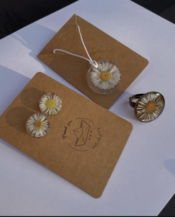 Collana, orecchini e anello con margherite pressate in resina, su sfondo bianco