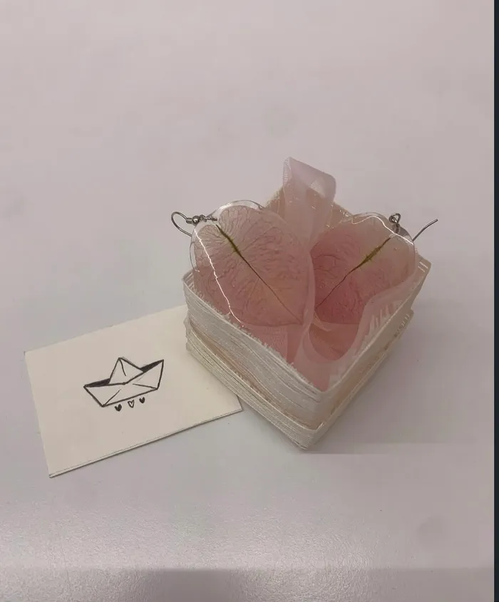 Mano che indossa un orecchino in resina con foglia rosa