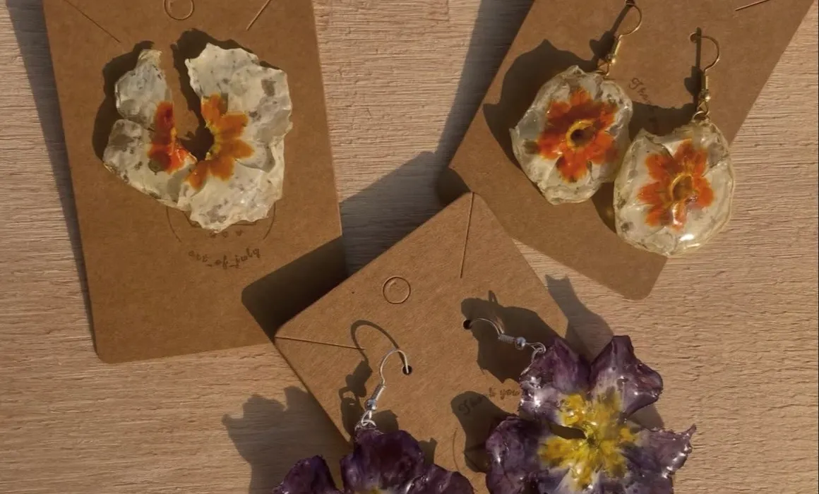 Orecchini con fiori pressati arancio e viola su un tavolo di legno