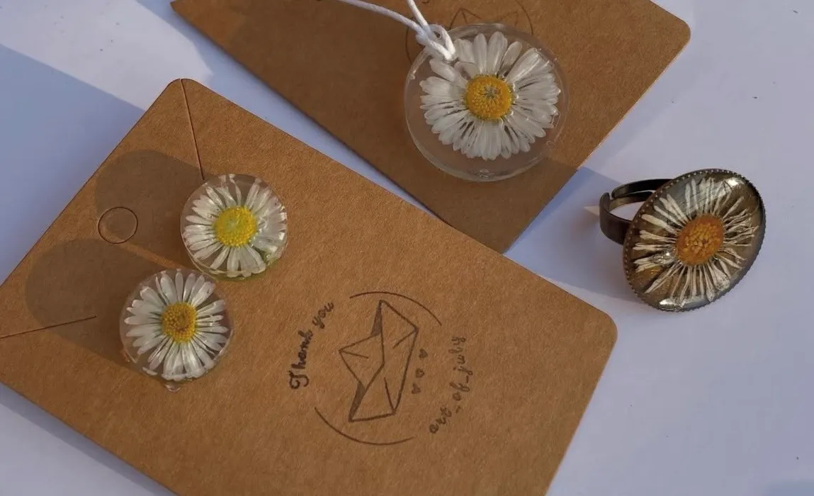 Collana, orecchini e anello con margherite pressate in resina, su sfondo bianco